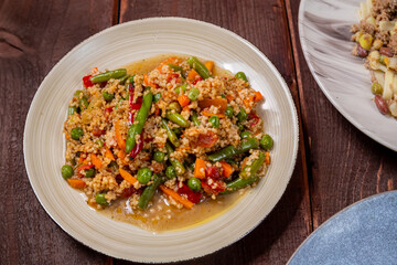Couscous with vegetables in spices in a plate on a wooden table