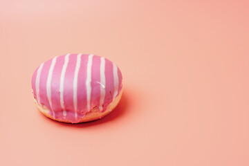 A pink and white donut with a white stripe on it. The donut is sitting on a pink background
