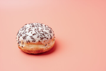 A donut with sprinkles on top. The donut is sitting on a pink background. The donut is the main focus of the image
