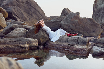 Serenity by the sea woman in white dress lounging on rocks with feet up in the air