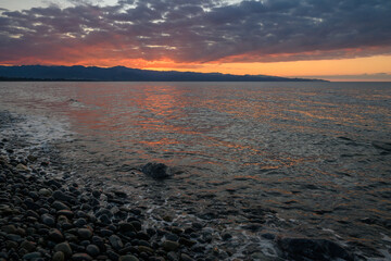 Vibrant sunset reflecting over calm waters along a rocky shoreline in a tranquil coastal setting