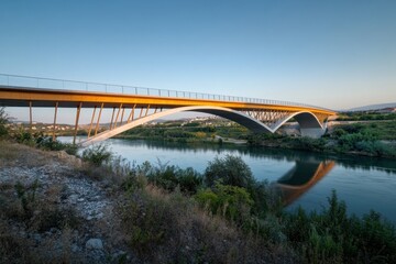 Obraz premium Sleek bridge design integrates with natural surroundings, beautifully illuminated by the sun at sunset