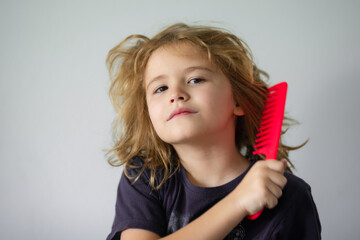 Closeup portrait of little child brushing hair isolated on gray studio background. Child with brush combing hair. Boy taking hairstyle. Child brushing hair with comb, kids haircare.