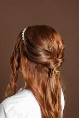 Teenage girl with stylish hair accessories on brown background, back view