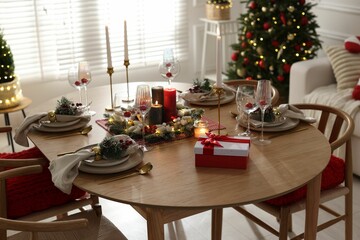 Christmas table setting with stylish dishware, glasses and burning candles in festive decorated room