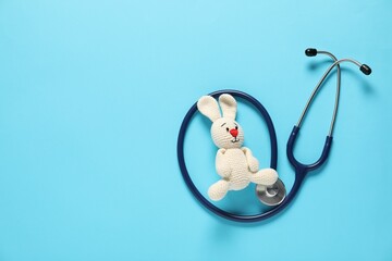 Pediatrics concept. Toy bunny with stethoscope on light blue background, top view. Space for text