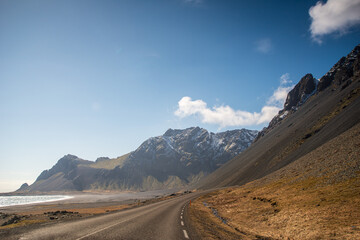 Coastal road winding through dramatic cliffs and black sand beaches, with the ocean glittering under the afternoon sun.