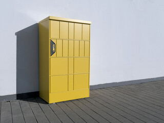 Yellow automatic parcel locker machine standing on the street in front of a white wall