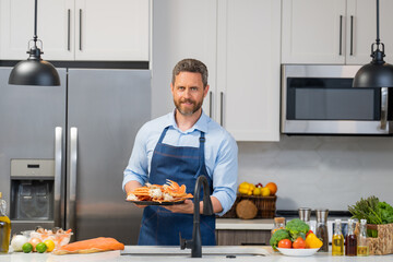 Man in cook apron preparing fish salmon at home modern kitchen. Handsome man is cooking fresh fish salmon seafood crab and shrimp and lobster in the kitchen.