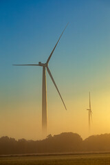 Fototapeta premium Vertical picture of two wind turbines in the fields of La Mancha, Spain, in a colorful sunrise