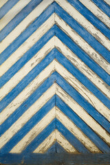 Puerta vieja de tablones de madera en diagonal pintados a rayas blancas y azules