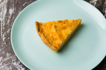 Flatlay, a piece of delicious open quiche pie with chicken, cheese and cream on a turquoise plate. Concept of food blog, writing recipes.