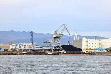Fototapeta premium Large crane works on large coal stockpile and container at Industrial port. Cargo transportation and activity at modern shipping container terminal.