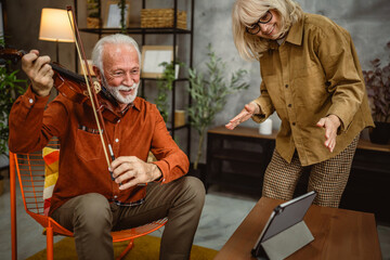 senior man learn to play violin at home on tablet and wife support him