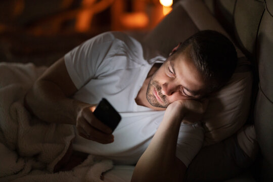 A man lying in bed at night and doom scrolling on social media ignoring sleep.