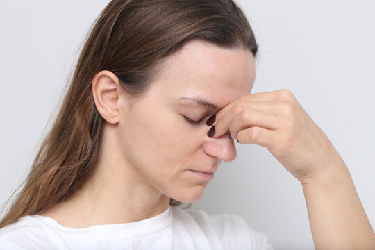 Woman holding her nose. Grimacing in pain from sinus pressure. Pain facial expression. Chronic sinus pain and headaches background. Difficulty of living with sinus issues and discomfort.