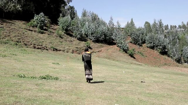 Steadicam shot of a woman carrying a large container of water through the countryside in rural Ethiopia.