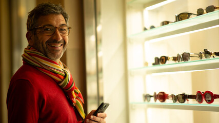 Smiling man holding smartphone near eyewear store display