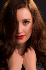 Portrait of a beautiful young woman with a serene expression, her long auburn hair covering one side of her face and hands holding onto the collar of her coat.