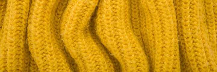Yellow wavy soft knitted fabric background. Closeup. Wide banner. Top down view.
