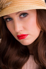 Vintage style portrait of a beautiful young woman with long auburn hair, wearing a beige summer straw hat.