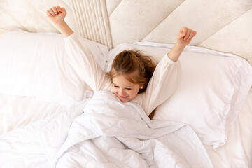 Cheerful little blonde girl in bed. Child woke up in bed with a good mood in the morning. textiles for the nursery. Have a nice day. Motherhood and childcare concept. High quality photo