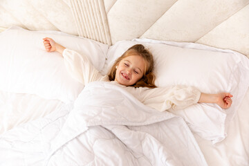 Cheerful little blonde girl in bed. Child woke up in bed with a good mood in the morning. textiles for the nursery. Have a nice day. Motherhood and childcare concept. High quality photo