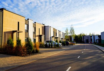Obraz premium Townhouse in residential district. New apartment buildings in green enviroment. Street with Townhouse along asphalt road in gated community. Car on parking at house. Modern Townhouses in suburban.