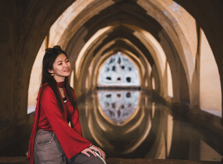 Portrait of a woman in red at the Alcazar of Seville, Spain, framed by Moorish arches and...