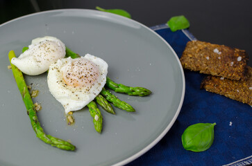 Breakfast and brunch ideas: poached eggs with asparagus in a plate with rye bread, top view