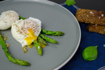 Breakfast and brunch ideas: poached eggs with asparagus in a plate with rye bread, top view
