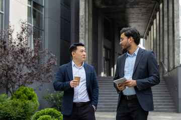 Two business colleagues walking down the street outside an office building, businessmen men in...