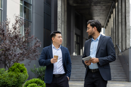Two business colleagues walking down the street outside an office building, businessmen men in business attire talking and discussing, on a lunch break.