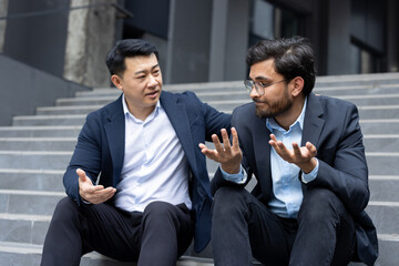 Supporting and comforting a partner, two men in business suits sitting on the stairs of an office building, a colleague helps a friend cope with frustration and anxiety.
