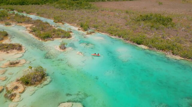 Toma a&eacute;rea de dron de una pareja de j&oacute;venes navegando tranquilamente en kayak en un r&iacute;o color turquesa de los R&aacute;pidos de Bacalar en M&eacute;xico