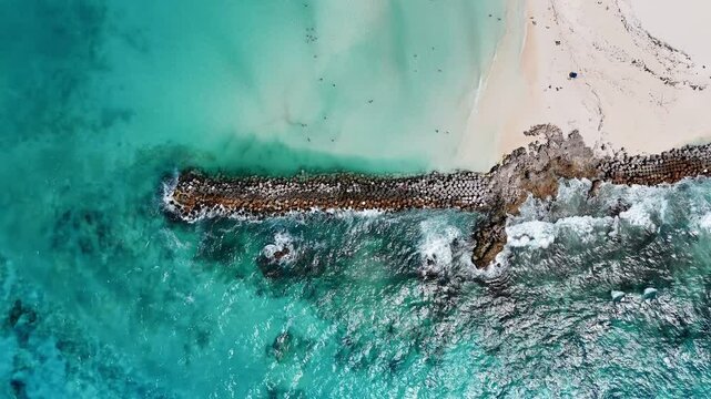 Toma a&eacute;rea cenital de dron volando sobre un rompeolas de rocas, en la playa y el mar turquesa de Canc&uacute;n