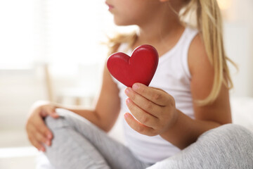 Orphanage concept. Little girl with red heart figure indoors, closeup