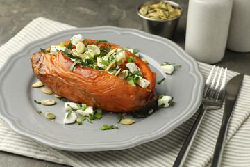 Tasty cooked sweet potato with feta cheese, pumpkin seeds and green onion on table, closeup