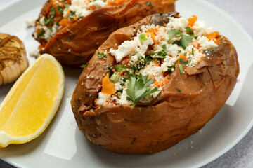 Tasty baked sweet potatoes with feta cheese, parsley and lemon slice on table, closeup