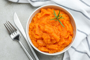 Tasty mashed sweet potato with rosemary in bowl served on grey textured table, flat lay