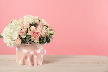 Beautiful bouquet in box on wooden table against pink background. Space for text