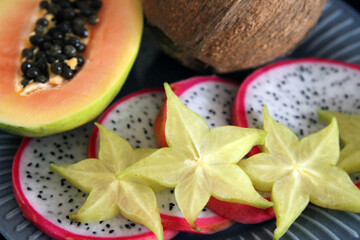 Coconut, papaya half, dragon fruit slices, carambola slices on the blue plate 