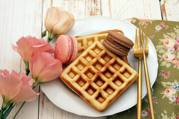 Breakfast with waffles and macaroons on the white plate in the wooden table