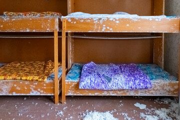 Abandoned dormitory with stained bedding and dust in a deserted building during daylight