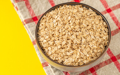 Bowl of raw rolled oats on a rustic cloth with yellow background, perfect for healthy eating or breakfast concepts.