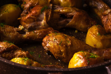 Roasted chicken legs with potatoes and dill in frying pan.