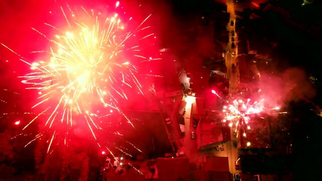 Spectacular New Year's Eve fireworks show captured by drone in a small town. Vibrant flashes of color light up the night sky, reflecting off nearby buildings and creating a magical atmosphere.