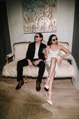 Stylish wedding couple relaxes on sofa, wearing sunglasses