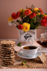 photo A cozy moment captured with a warm cup of black tea, surrounded by colorful flowers and a stack of delicious crisp cookies, setting a perfect scene for relaxation.