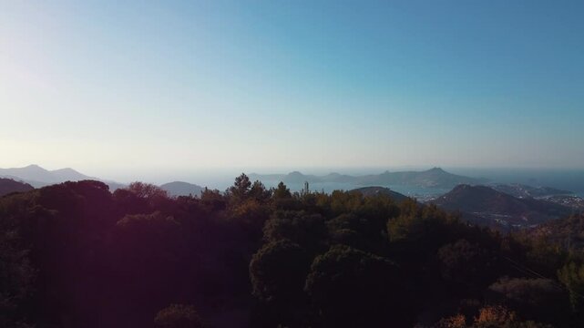 A breathtaking drone video starting from a forested hill and extending towards the sea. Hills covered with greenery, deep blue sea and islands in the distance, Bodrum Yalıkavak location.